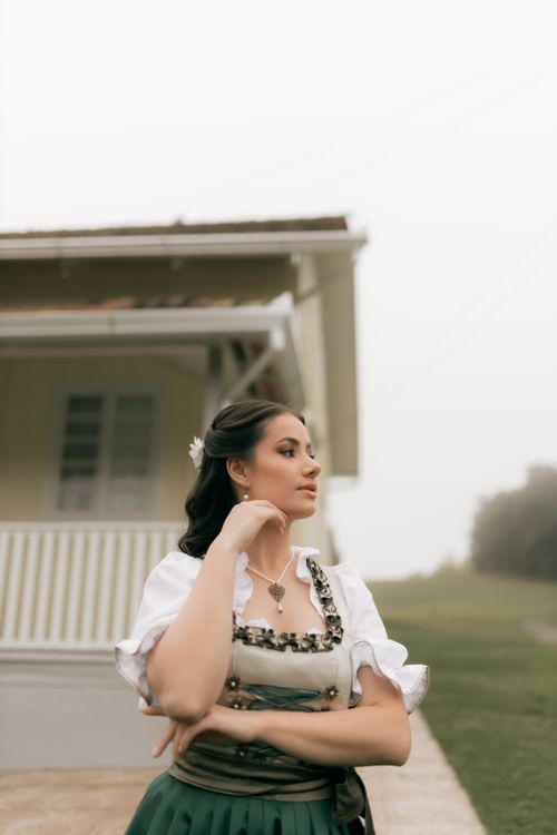 Free A young woman in traditional Bavarian outfit standing confidently outdoors by a house. Stock Photo
