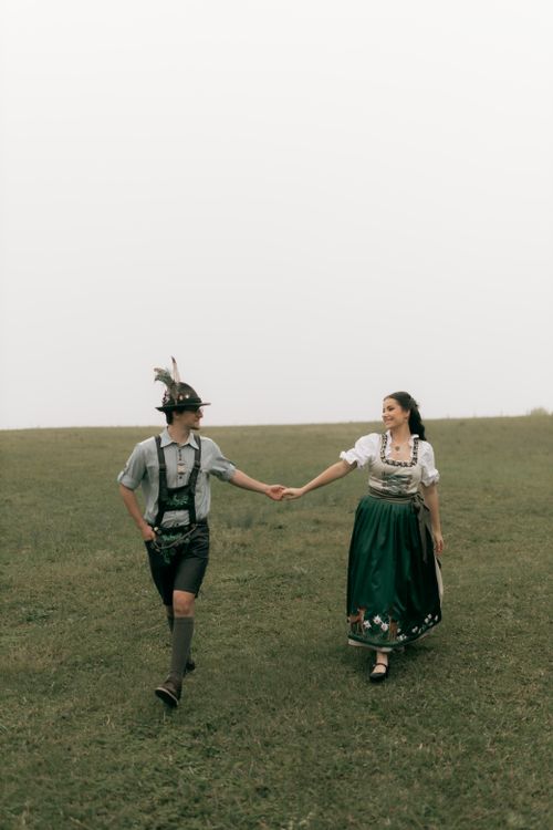 Free Couple in traditional Bavarian clothing enjoying a stroll on a grassy field during the day. Stock Photo
