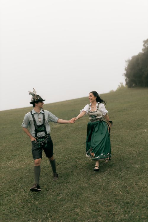 Free A couple in traditional Bavarian clothing holding hands on a grassy hill. Stock Photo