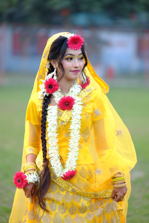 Free A bride in vibrant yellow traditional attire adorned with floral garlands, captured outdoors. Stock Photo