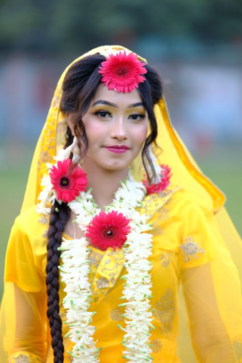 Free Portrait of a young woman in vibrant yellow traditional attire adorned with floral accessories. Stock Photo