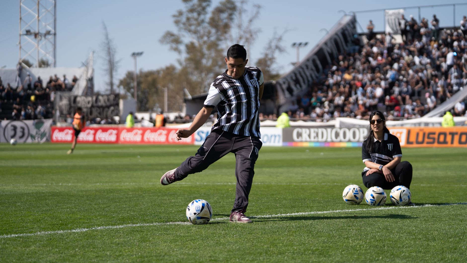 A football player kicks the ball during a match in a packed stadium.
