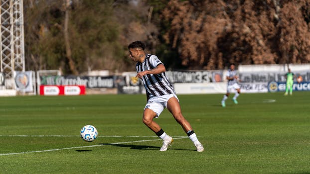 Soccer player in action kicking a ball on an outdoor field during the day.