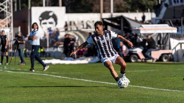 Dynamic shot of a footballer in action on the field during a sunny day match with spectators.