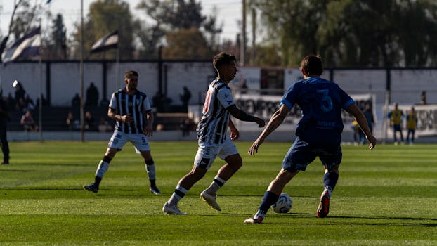 Players compete in a dynamic soccer match under clear skies on a grassy field.