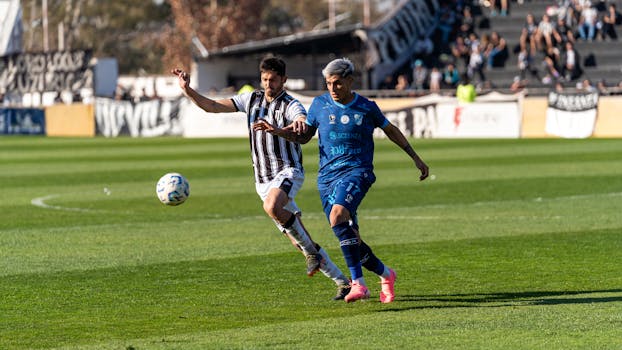 Two football players compete fiercely during a match on a bright sunny day.