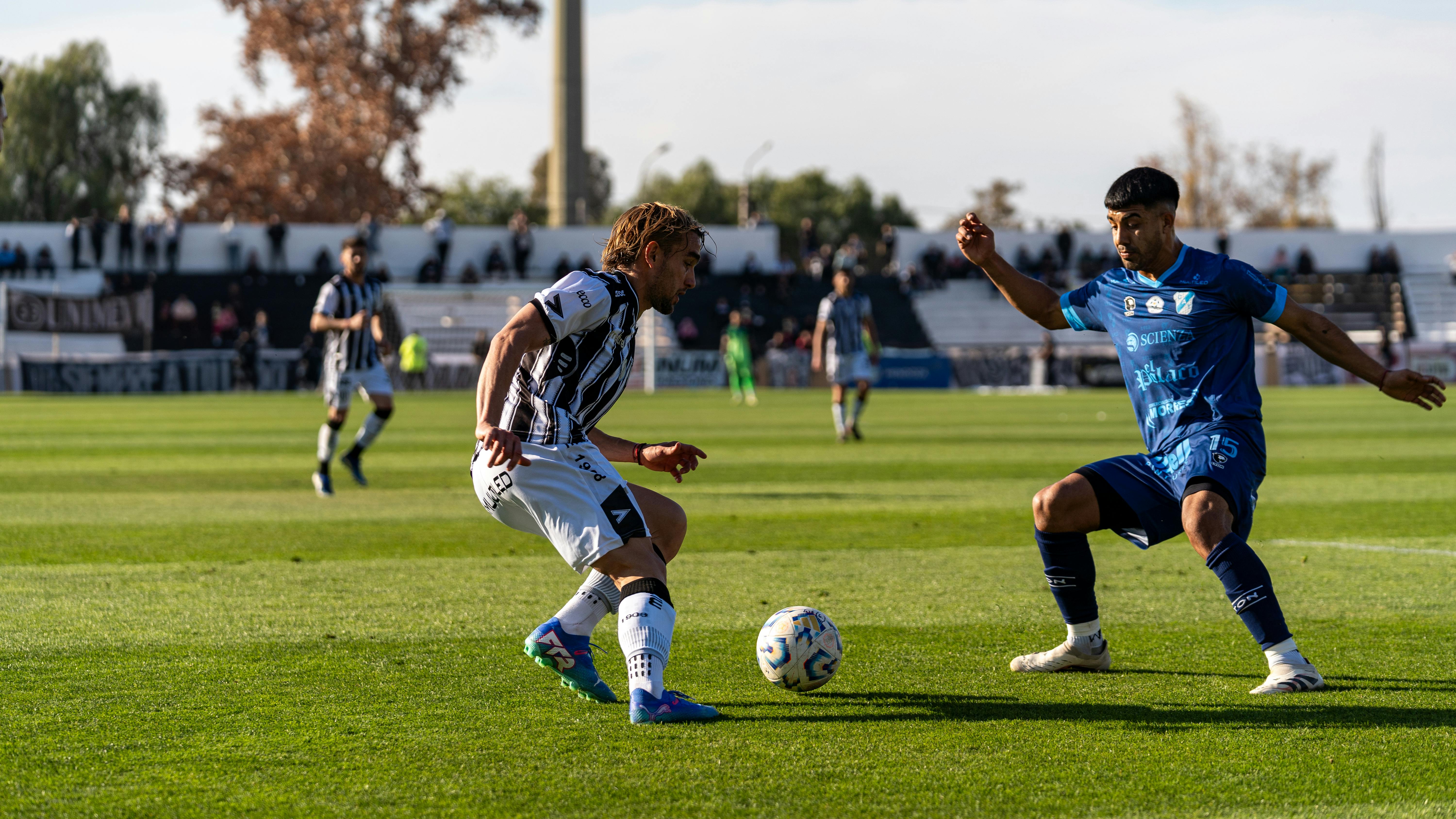 Two soccer players competing intensely during a match on a sunny day outdoors.