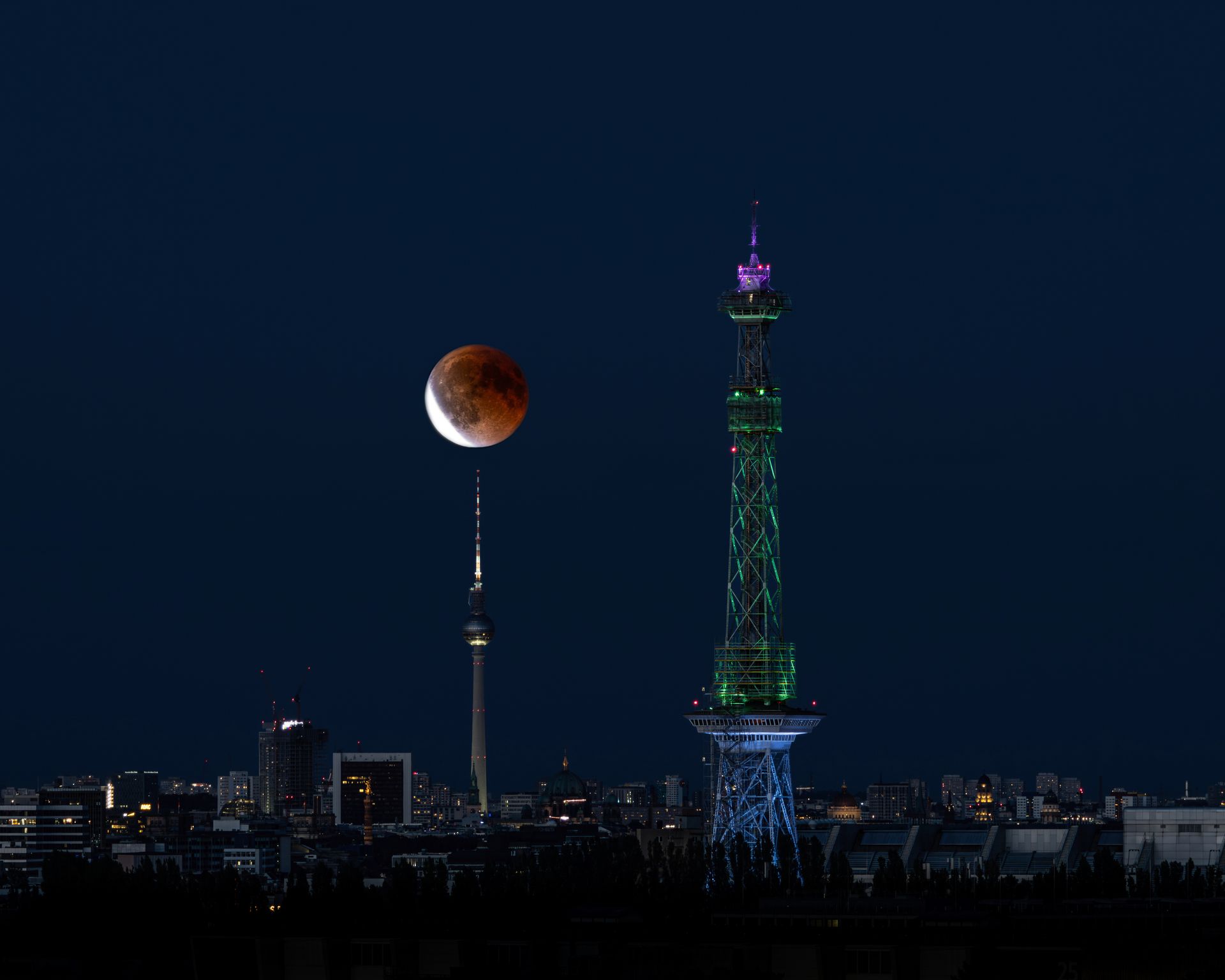 Capture of a lunar eclipse over the Berlin skyline featuring the moon, TV Tower, and Funkturm at night.