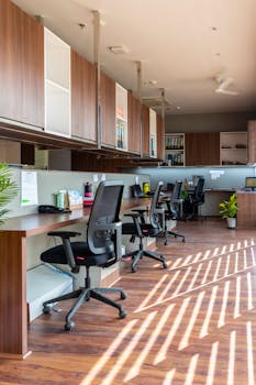 Bright and spacious open office with wooden desks and chairs under natural light. Ideal for creative workspaces.