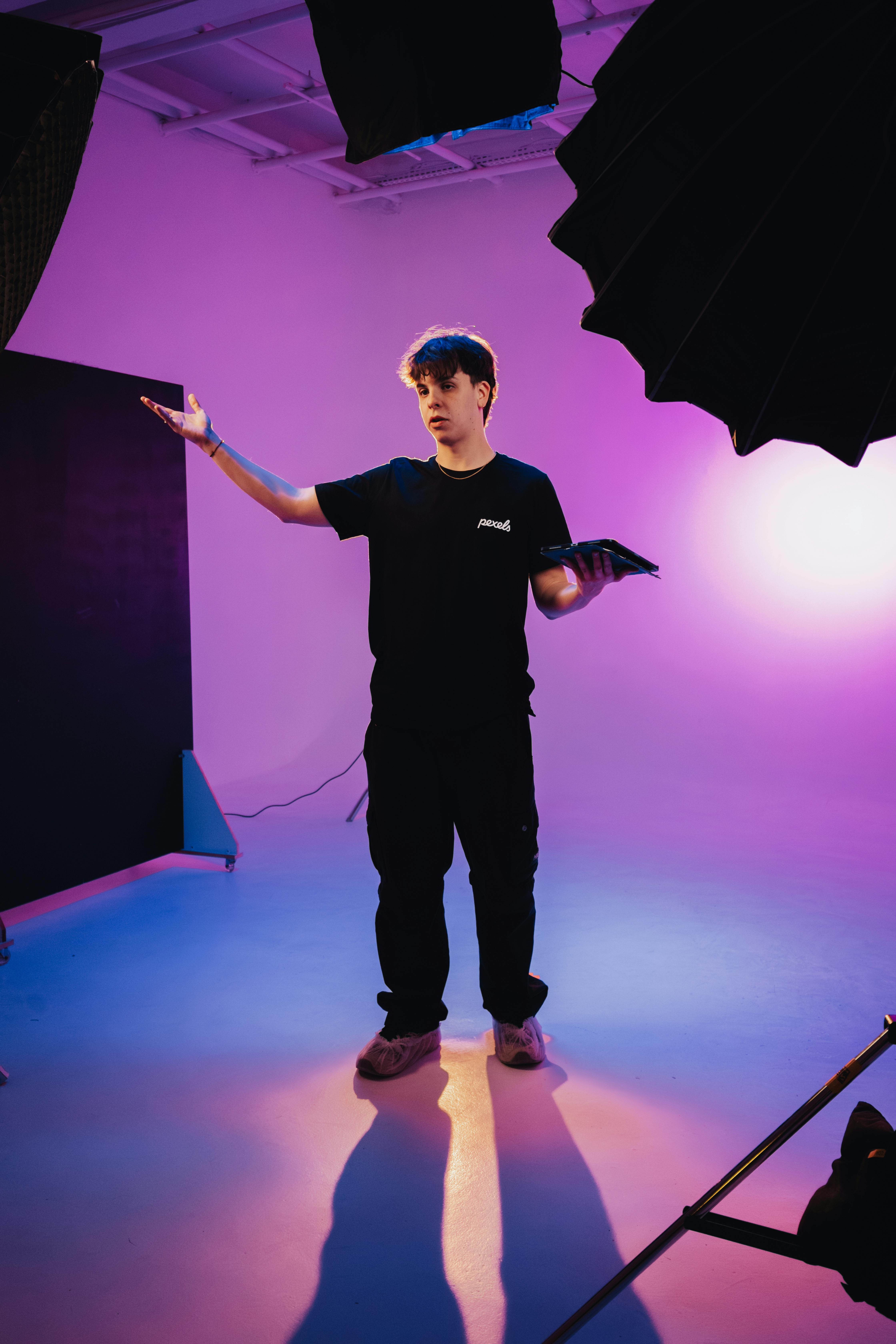 A young man stands in a vibrant photography studio setup with colorful lighting and equipment.