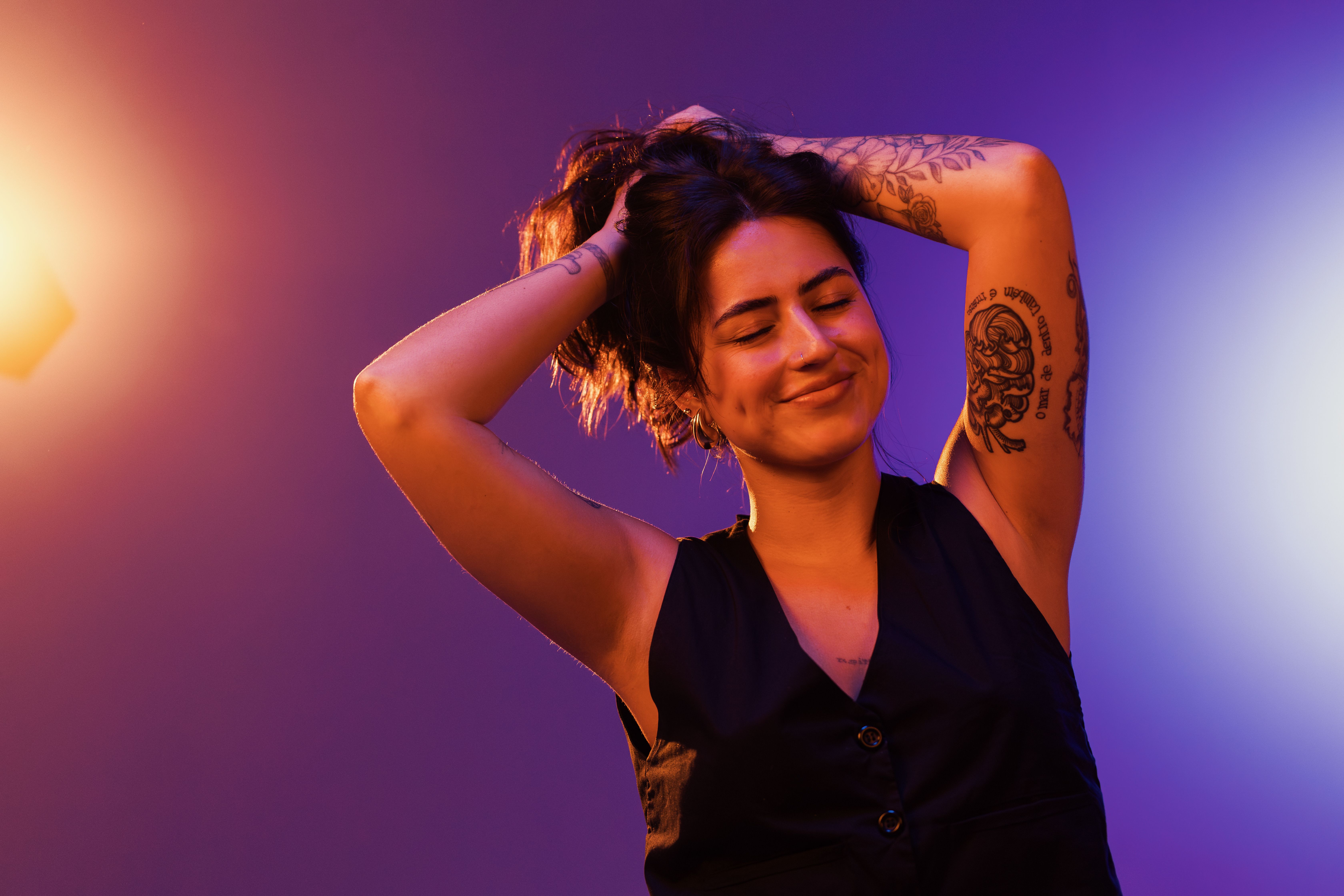 Femme souriante avec des tatouages posant sous des lumières de studio vibrantes, rayonnant de bonheur.