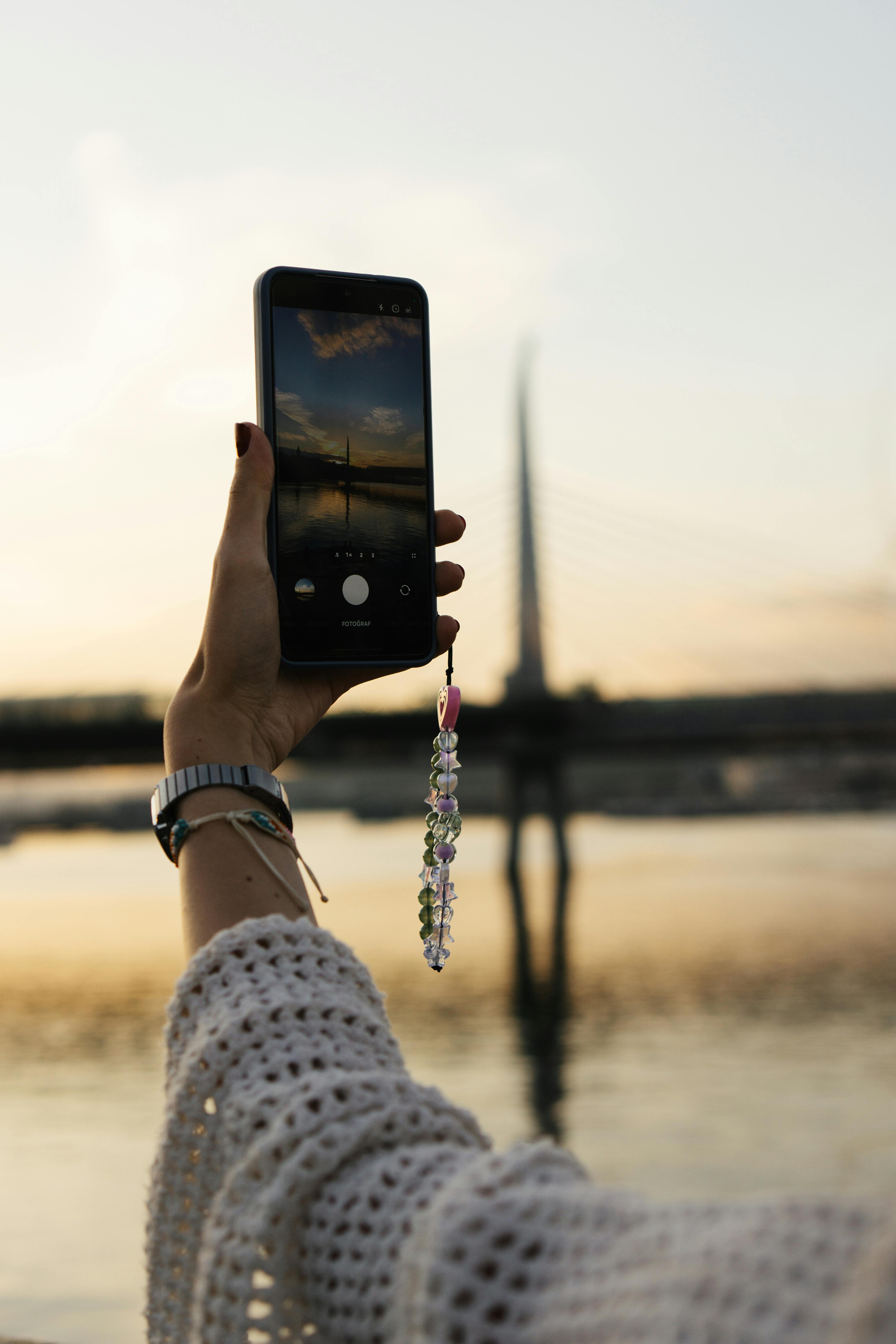 Free A person photographs Istanbul's skyline at sunset by the water. Iconic bridge in view. Stock Photo