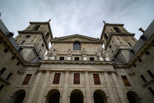 Low-angle view of El Escorial's historic facade under a cloudy sky, featuring classic architecture.