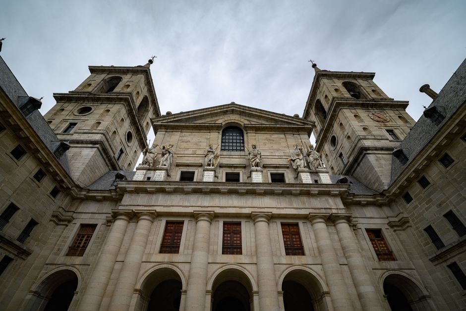 Low-angle view of El Escorial's historic facade under a cloudy sky, featuring classic architecture.