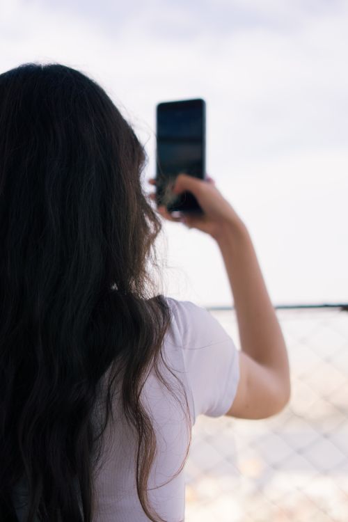 Free A woman takes a photo with her smartphone outdoors in İstanbul, capturing the view on a sunny day. Stock Photo
