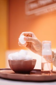 Close-up of a hand picking a cotton ball with warm lighting and skincare product.