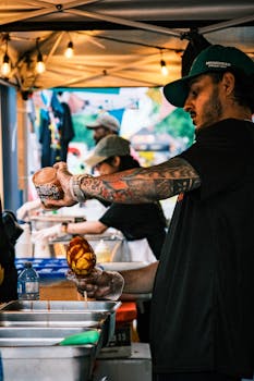 Street vendor in Toronto prepares food, adding sauce to a dish in a vibrant market setting.