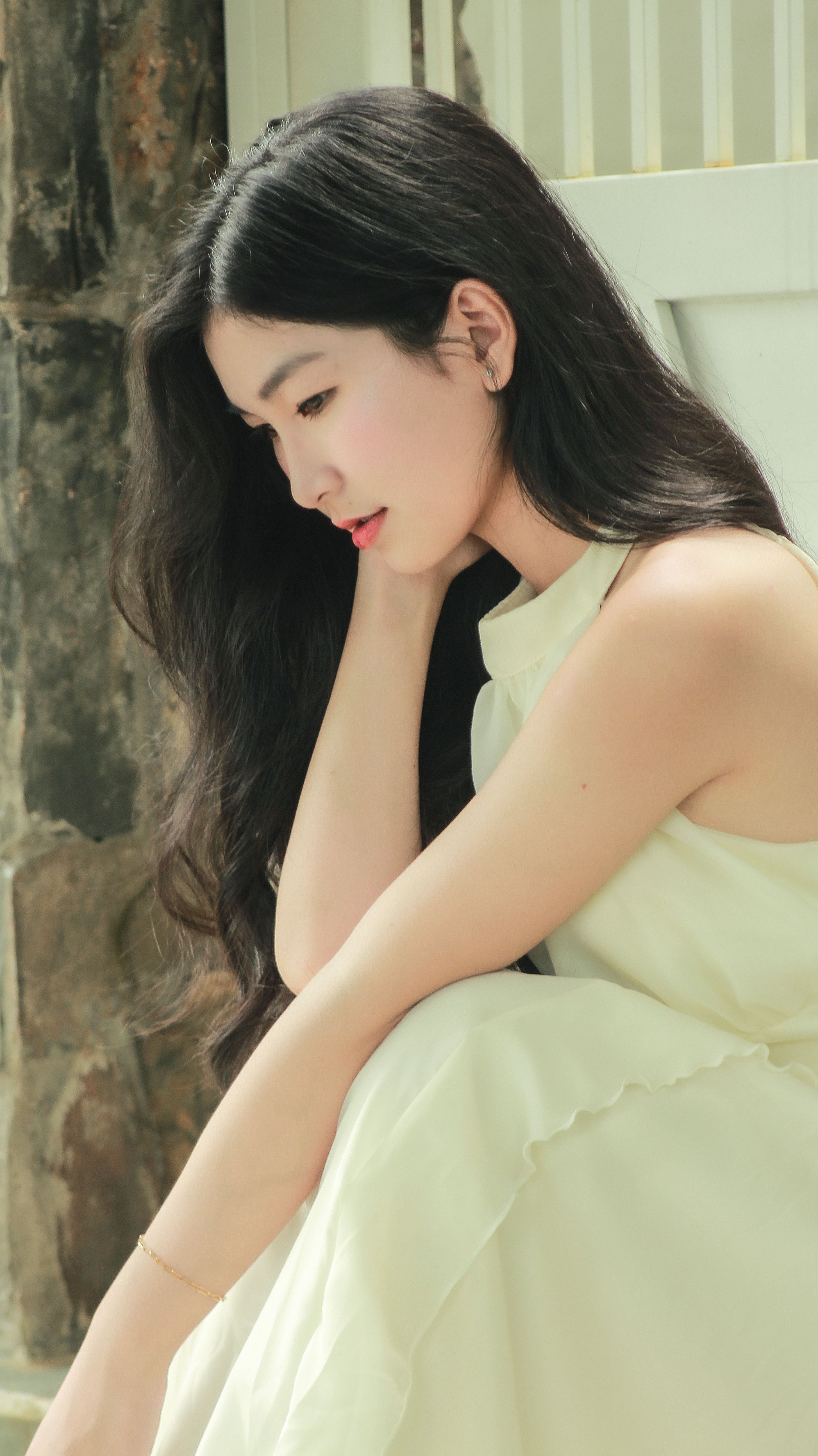 Side profile of a woman in a white dress, seated thoughtfully indoors.