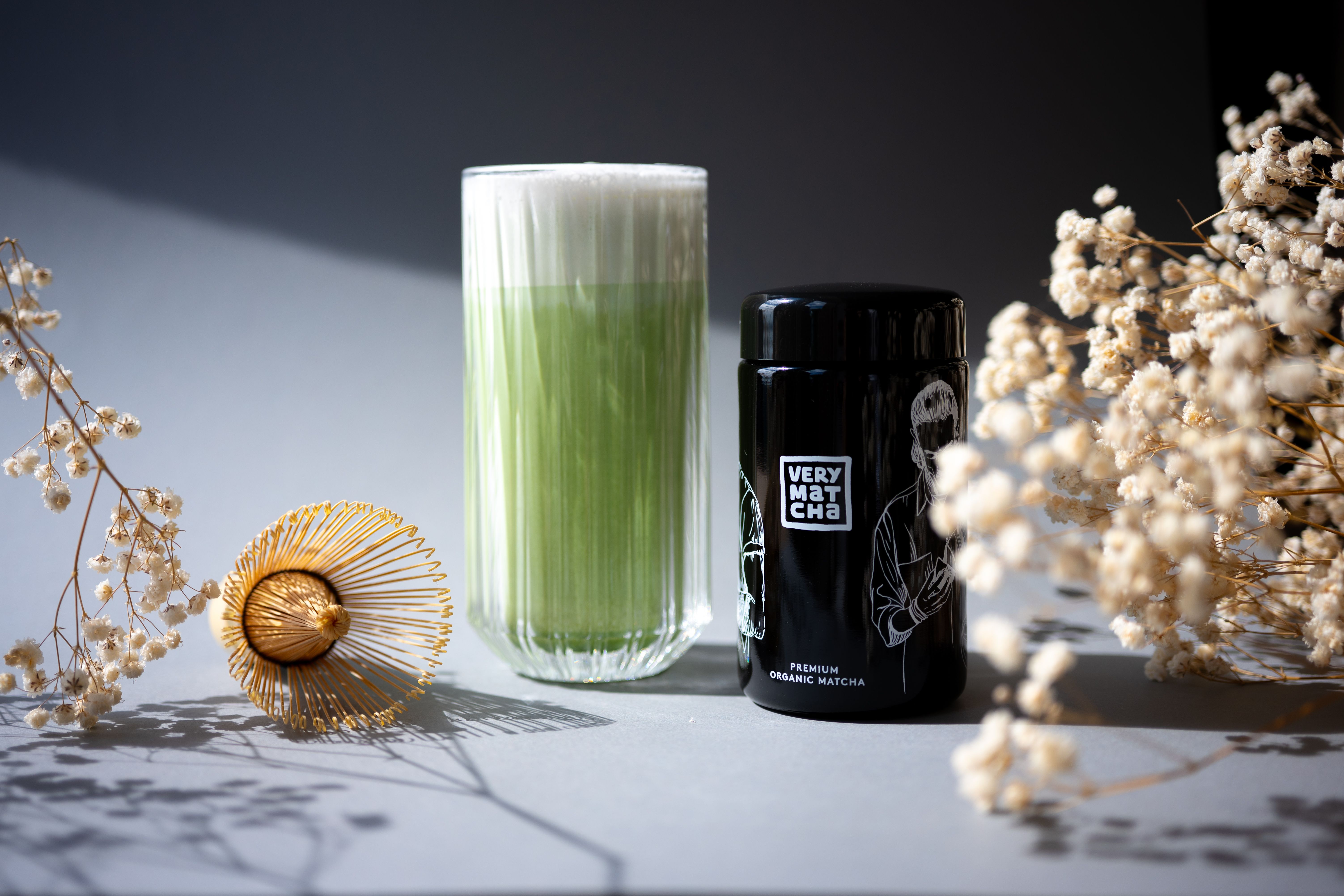 A stylish display of matcha latte with bamboo whisk and tea canister, adorned by soft florals.