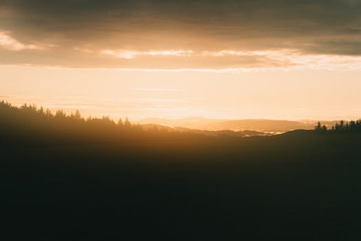 Silhouette of forested hills under a warm golden sunset with dramatic clouds.