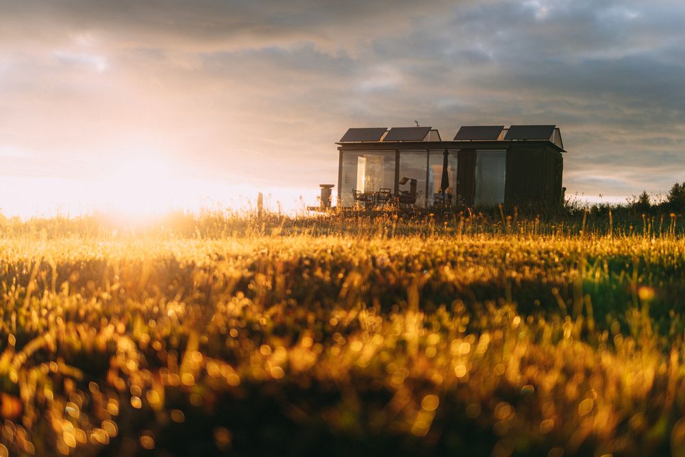 A compact house with roof-mounted solar panels standing in a field at sunset — photo by merwak. raw on Pexels
