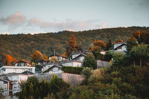 Free Charming hillside houses amidst lush green trees under a clear sky. Perfect representation of serene living. Stock Photo
