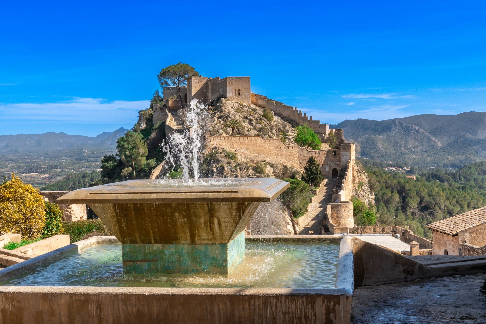 Explore the historic Xàtiva Castle in Spain, featuring a stunning outdoor fountain and mountainous backdrop.
