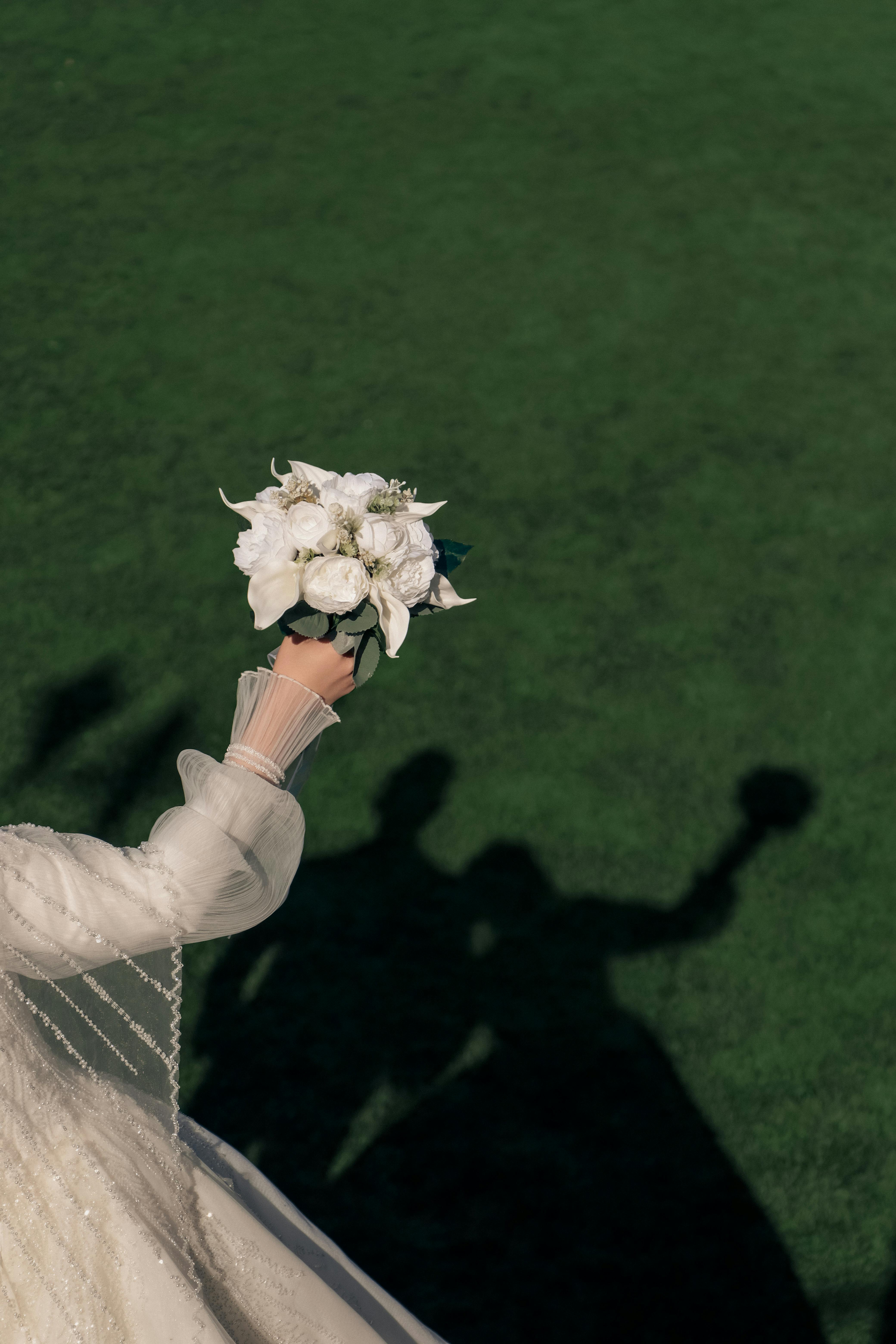Bride holding bouquet with shadows on grass, perfect for outdoor wedding themes.