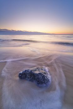 Captivating sunset on Hjørring beach with a solitary rock and gentle waves.