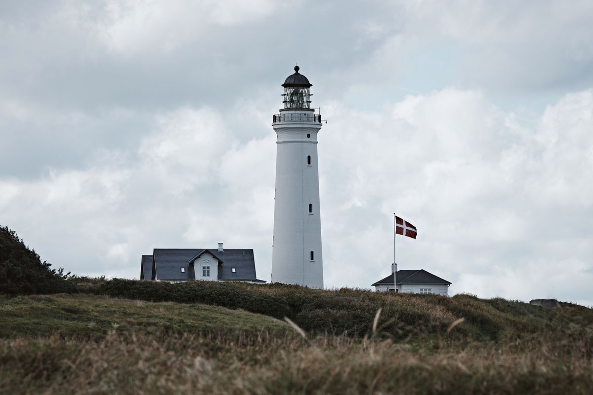 White lighthouse with a Danish flag on a grassy headland