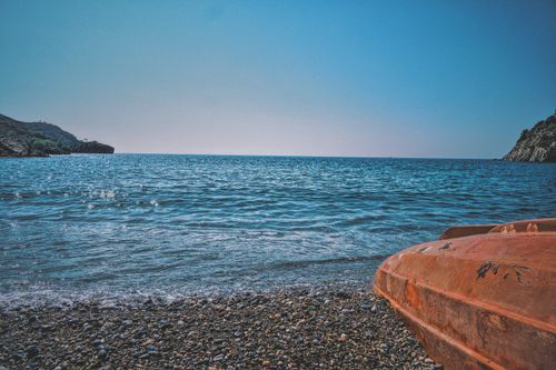 Free Serene beach view with a calm sea, rocky shore, and an orange kayak in the foreground. Perfect for relaxation themes. Stock Photo