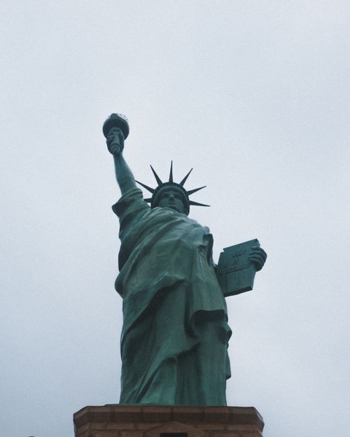 Free View of the iconic Statue of Liberty in New York against a gray, overcast sky. Stock Photo