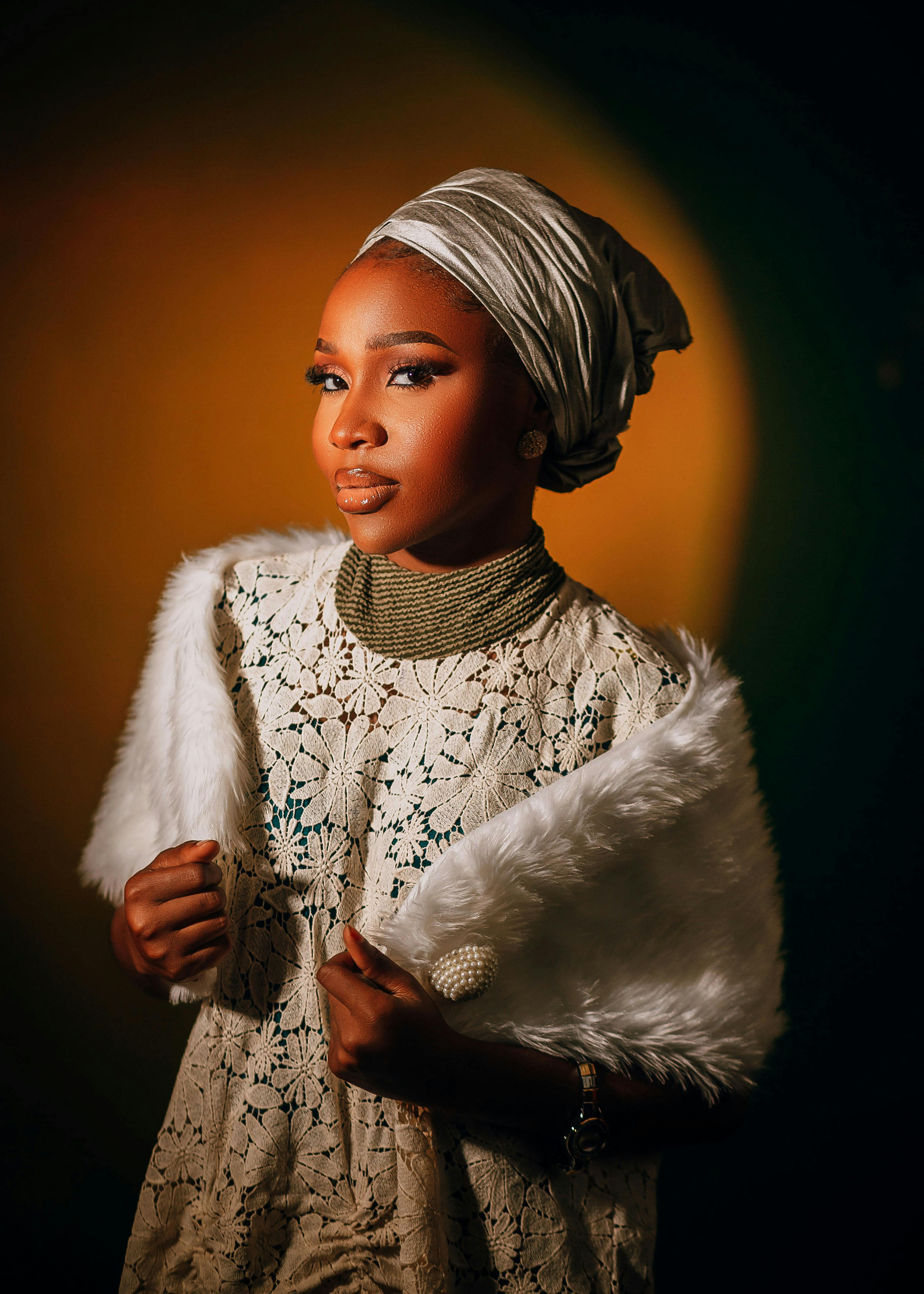 gratis Een vrouw in traditionele kledij en hoofddoek poseert elegant tegen een warme achtergrond. Stockfoto