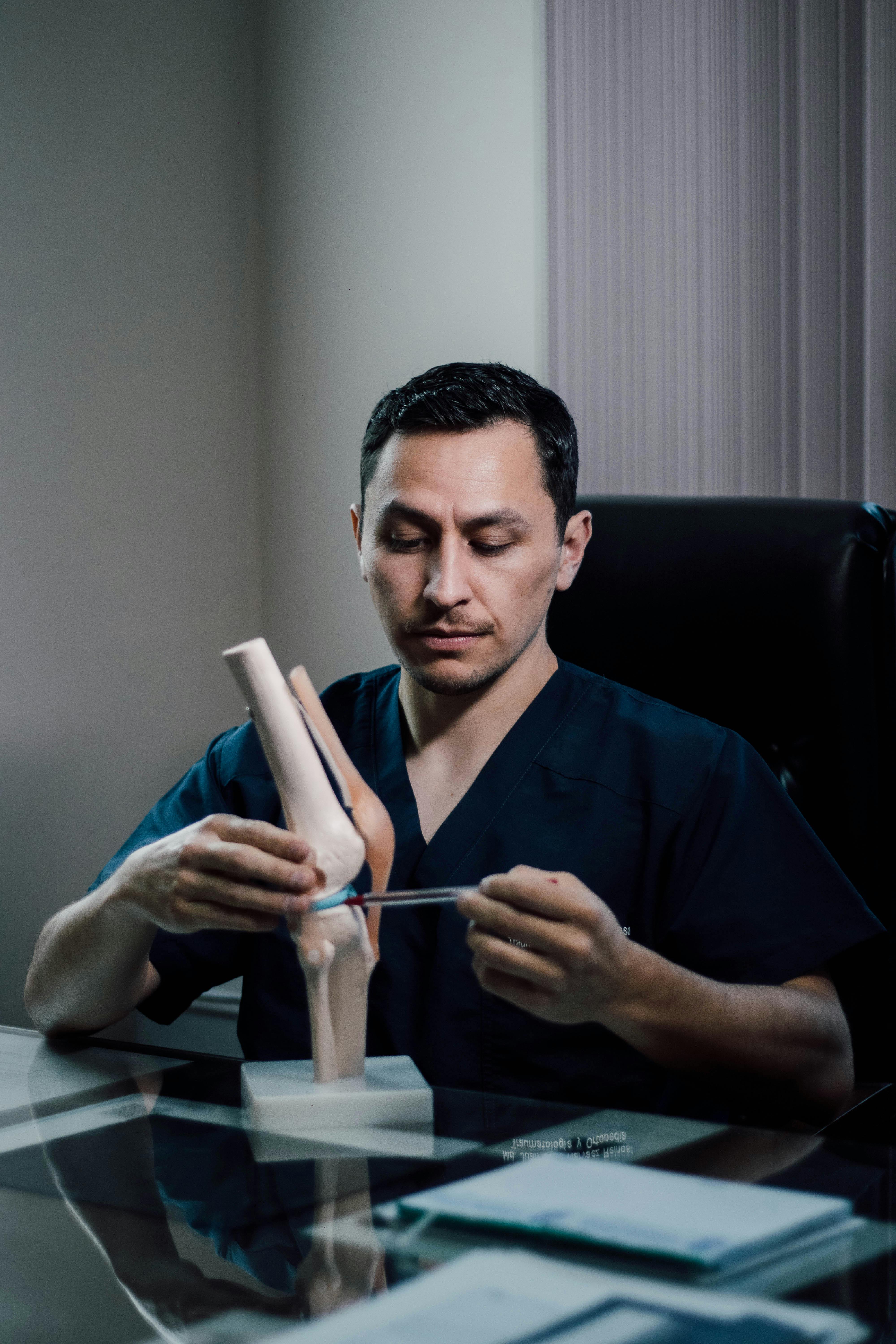 Bezpłatne Lekarz wyjaśnia anatomię kolana za pomocą modelu w gabinecie, podkreślając swoją wiedzę ortopedyczną. Zdjęcie z galerii