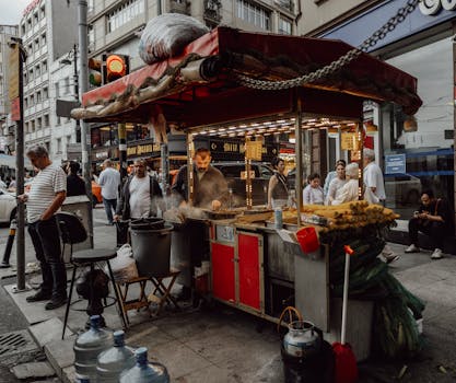 Street vendor prepares grilled corn and chestnuts on a busy urban street, attracting passersby.