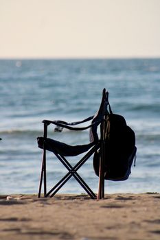 A solitary camping chair facing the sea on a tranquil sandy beach.