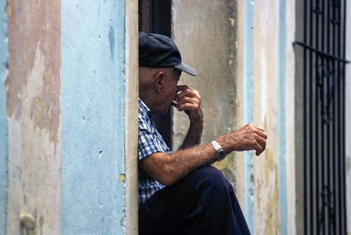 Free Portrait of an elderly man sitting in a doorway in Cuba, capturing a moment of reflection. Stock Photo