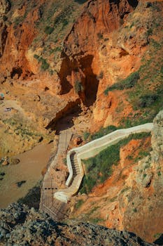 Aerial view of a winding path through vibrant red cliffs by the seaside, offering a striking natural scene.