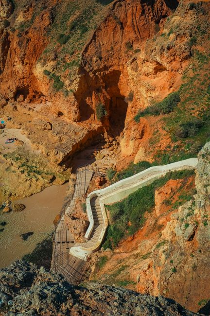 Aerial view of a winding path through vibrant red cliffs by the seaside, offering a striking natural scene.