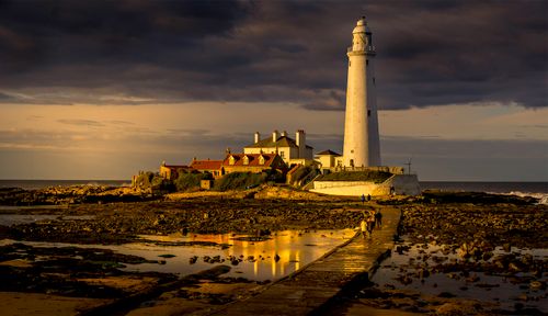 Free Scenic view of St. Mary's Lighthouse, UK at sunset, with dramatic clouds and rocky shores. Stock Photo