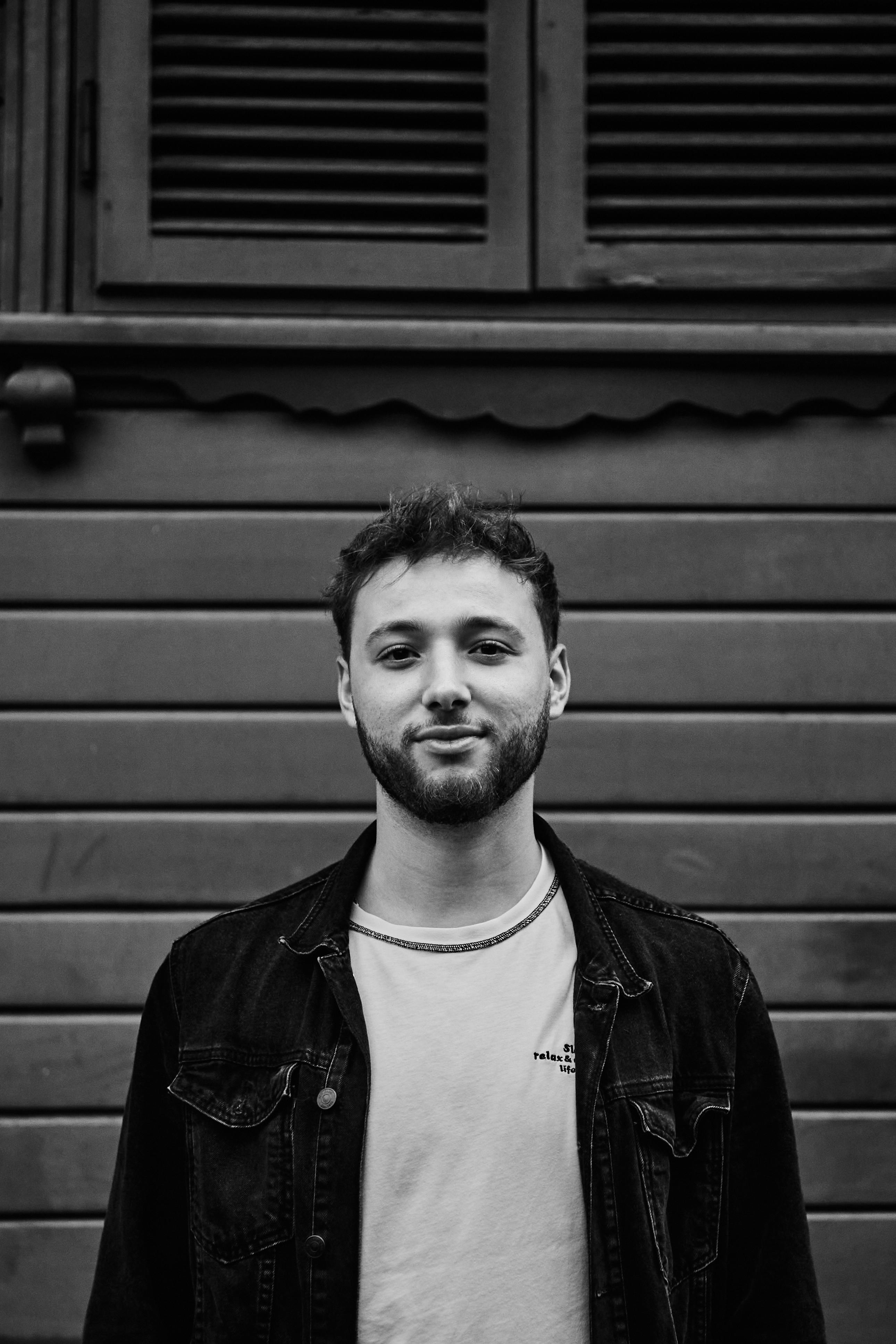 Black and white portrait of a young man posing casually against a wooden wall in Istanbul, Türkiye.