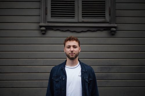 Free Young man in denim jacket standing against a wooden wall in Istanbul, displaying a casual and thoughtful expression. Stock Photo
