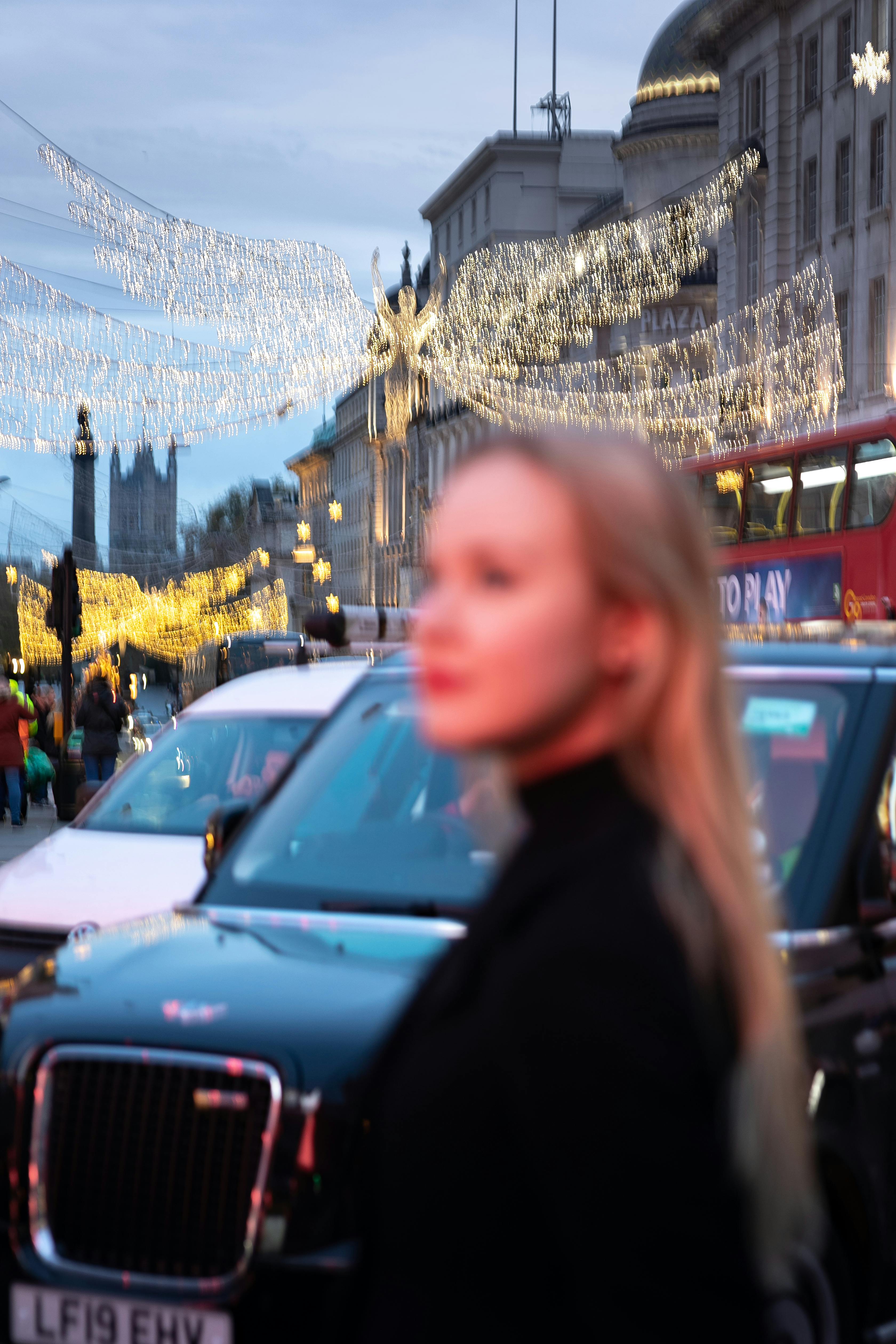 Blurred view of a woman on a busy London street adorned with sparkling Christmas lights.
