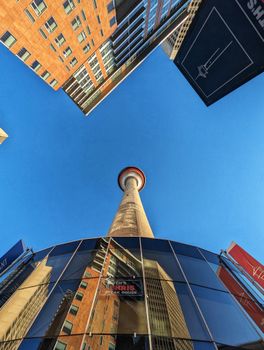 Upward view of the iconic Calgary Tower surrounded by tall buildings in vibrant daylight.