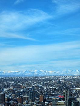 Cityscape with snow-capped mountains under a bright blue sky.