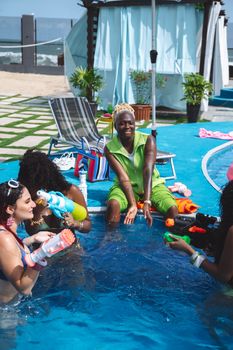 Group of friends having fun in a pool with water guns on a sunny day.
