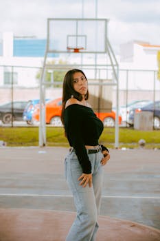 Stylish woman posing on an outdoor basketball court with urban background.