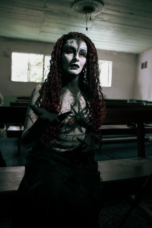 Free Gothic figure with haunting makeup and costume in a dimly lit room with benches. Stock Photo