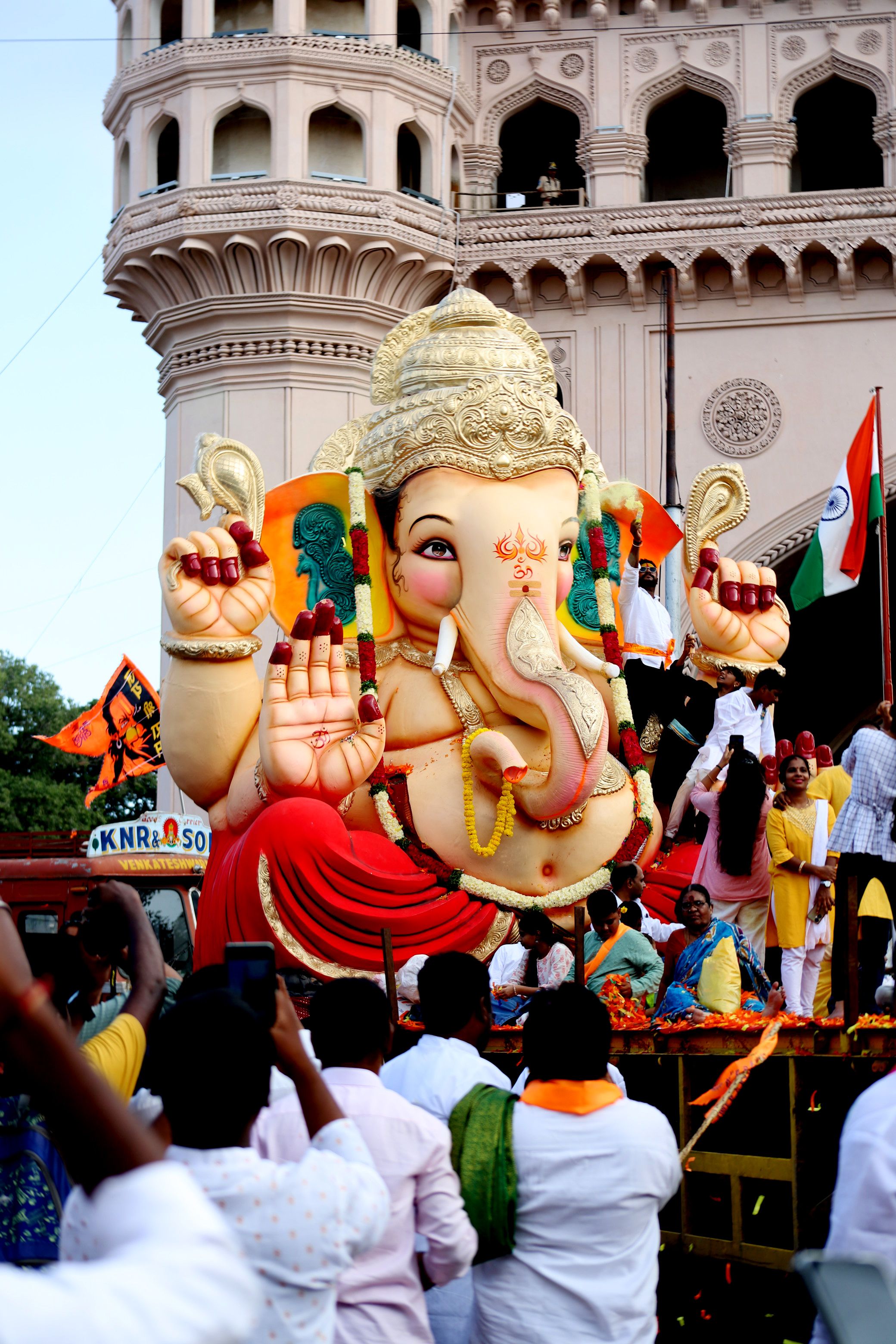 Vibrant Ganesh idol procession during a festival in India with a traditional backdrop.