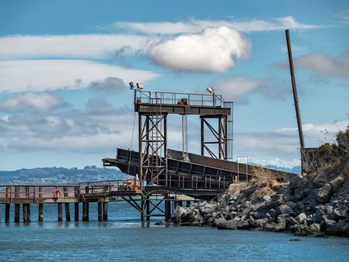 Free A rustic waterfront structure on a rocky shoreline under a clear blue sky with scattered clouds. Stock Photo